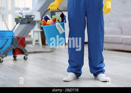 Jeune homme tenant le seau avec l'équipement de nettoyage et les fournitures à l'intérieur Banque D'Images