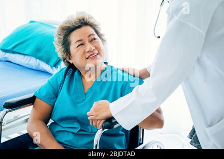Une patiente âgée souriante assise sur un fauteuil roulant regarde un médecin de l'hôpital ou de la clinique Banque D'Images