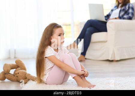 Une petite fille triste assise au sol dans la chambre Banque D'Images