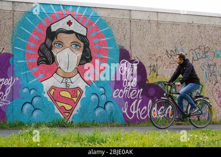 Hamm/Allemagne, 29 avril 2020: Poéple passant un graffiti de coronavirus par l'artiste de rue Kai „Uzey“ Wohlgemuth montrant 'Super-Nurse' avec un masque de protection sur un mur à Hamm, Allemagne. L'écriture Sainte dit: "Pour les vrais héros" --- Hamm, 29.4.2020 - Corona-Kunst. DAS Graffiti „Super-Nurse“ une einer Wand à Hamm. Eine Krankenschwester mit Mundschutz und Supermann-logo chapeau der Graffiti-Künstler Kai „Uzey“ Wohlgemuth aus Hamm den echten Helden in der Corona-KRise gewidmet. Banque D'Images