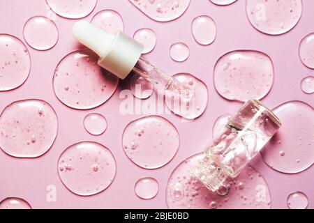 Gouttes de gel liquide ou de sérum avec pipette sur fond rose en macro. Style plat. Banque D'Images
