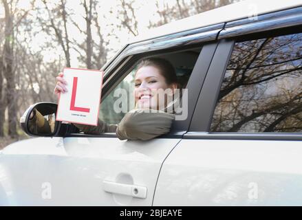 Une jeune femme tenant le panneau conducteur de l'apprenant en regardant hors de la fenêtre de voiture Banque D'Images