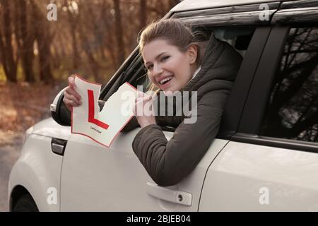 Une jeune femme déchirant le panneau conducteur de l'apprenant tout en regardant hors de la fenêtre de voiture Banque D'Images