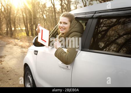 Une jeune femme tenant le panneau conducteur de l'apprenant en regardant hors de la fenêtre de voiture Banque D'Images