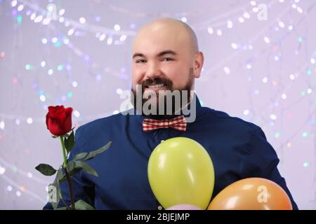 Homme de graisse drôle avec des ballons et des fleurs à la fête d'anniversaire Banque D'Images