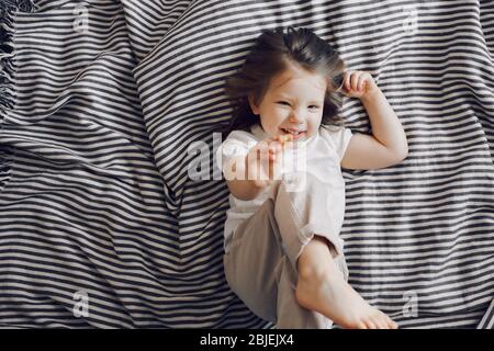 Portrait de belle petite fille de 3 ans posée sur le lit en robe et regardant l'appareil photo Banque D'Images