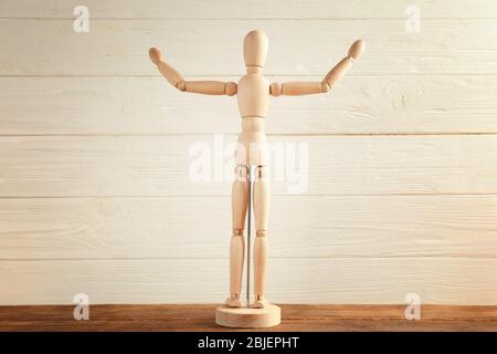 Mannequin en bois avec mains levées sur la table, fond clair Banque D'Images