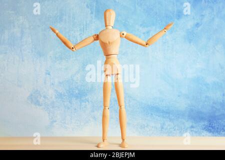 Mannequin en bois avec mains levées sur la table, fond clair Banque D'Images