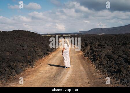 Femme avec robe blanche marche sur le chemin des formations rocheuses volcaniques à Lanzarote, îles Canaries, Espagne Banque D'Images