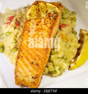 Saumon poêlé servi avec du risotto au citron. Le plat est garni de citron grillé. Banque D'Images