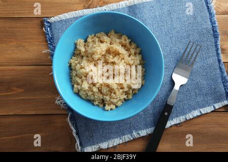 Vue de dessus de la plaque bleue avec des grains de quinoa biologique bouillis spassés sur fond de bois Banque D'Images