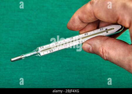 Un thermomètre au mercure en verre indique la température élevée du corps humain sur son échelle. La main de l'homme tient un outil médical de diagnostic ou un appareil de mesure, Banque D'Images