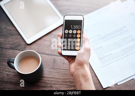 Personne utilisant une calculatrice sur un téléphone portable avec un café dans la prise sur un bureau Banque D'Images