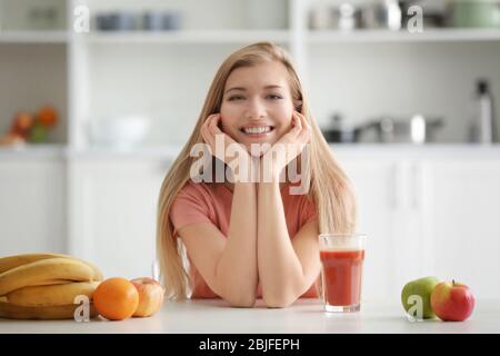 Jeune femme avec un verre de jus frais à la cuisine Banque D'Images