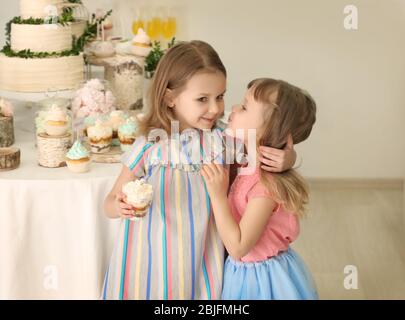 Mignons petites filles près de la table avec des bonbons servis pour la fête Banque D'Images