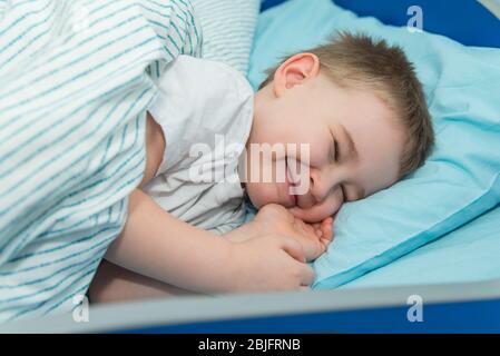 Un petit garçon s'y couche et prétend qu'il dormait. Un enfant souriant au lit Banque D'Images