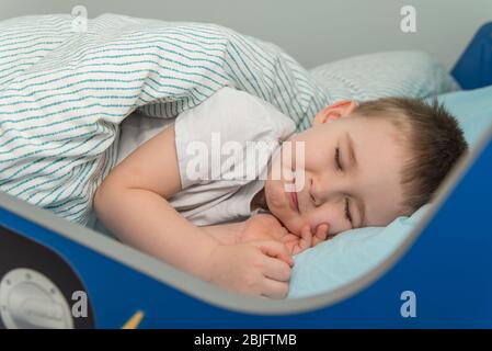 Un petit garçon s'y couche et prétend qu'il dormait. Un enfant souriant au lit Banque D'Images