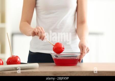 Femme tenant la pomme de bonbons sur le bâton au-dessus de la cuvette de verre avec le caramel Banque D'Images