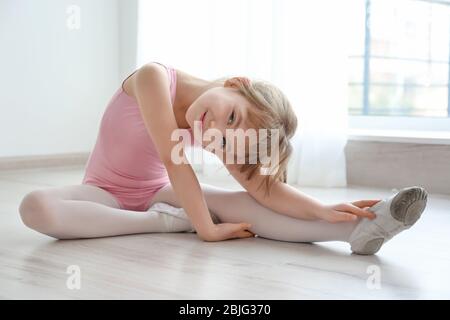 Joli petit ballerina assis sur le sol dans un studio de danse Banque D'Images