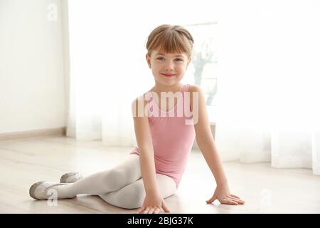 Joli petit ballerina assis sur le sol dans un studio de danse Banque D'Images