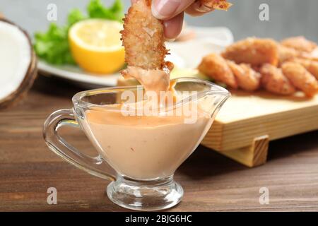 Main féminine trempant de délicieuses crevettes à la noix de coco dans la sauce, à proximité Banque D'Images