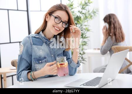 Belle jeune femme avec limonade et ordinateur portable dans le café Banque D'Images