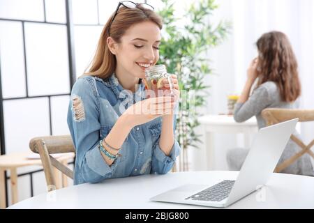 Belle jeune femme avec limonade et ordinateur portable dans le café Banque D'Images