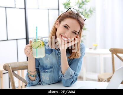 Belle jeune femme avec limonade et ordinateur portable dans le café Banque D'Images