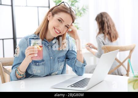 Belle jeune femme avec limonade et ordinateur portable dans le café Banque D'Images