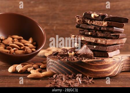 Planche à découper avec tas de chocolat, bol et noix sur fond en bois Banque D'Images