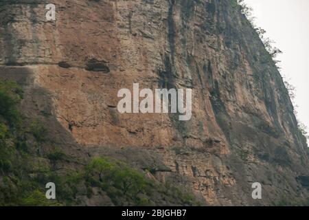 Wuchan, Chine - 7 mai 2010 : Dawu ou Misty gorge sur la rivière Daning. Grottes avec cercueils de personnes tribales anciennes se hewn dans la falaise brune. Un peu de feuillage chez le bot Banque D'Images