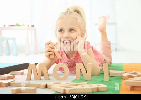 Jolie petite fille et mot MONI composé de lettres en bois sur le plancher à la maison Banque D'Images