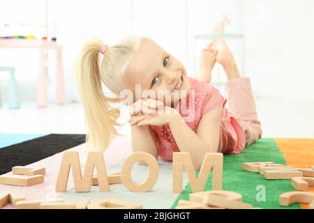 Jolie petite fille et mot MOM composé de lettres en bois sur le plancher à la maison Banque D'Images