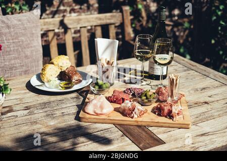 Carte de charcuterie servie avec du vin blanc à l'extérieur. Un plateau de tranches de jambon et de bacon avec des cornichons sur une planche de bois Banque D'Images