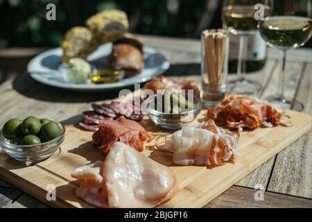 Gros plan du tableau de la Charcuterie servi avec du vin blanc à l'extérieur. Un plateau de tranches de jambon et de bacon avec des cornichons sur une planche de bois Banque D'Images