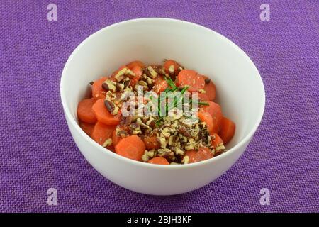 Tranches de carottes cuites avec des noix et des ciboulettes dans un bol à plat blanc sur une nappe violette Banque D'Images