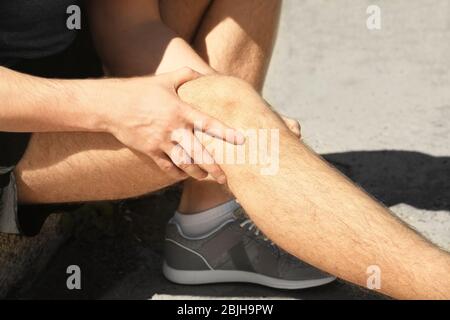 Jeune homme souffrant de douleur dans la jambe dehors, closeup Banque D'Images