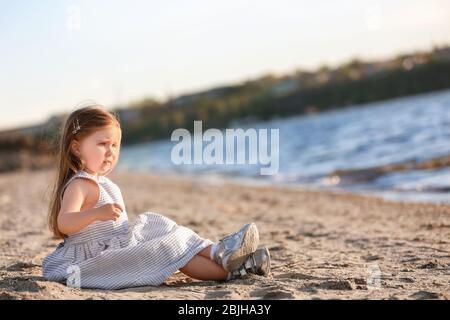 Petite fille mignon assise près de la rivière Banque D'Images