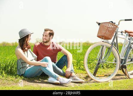 Un jeune couple heureux avec un vélo assis sur l'herbe dans le champ Banque D'Images