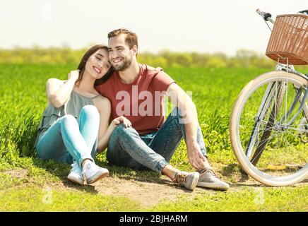 Un jeune couple heureux avec un vélo assis sur l'herbe dans le champ Banque D'Images