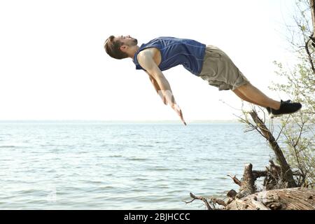 Jeune homme sportif faisant des exercices acrobatiques près de la rivière Banque D'Images