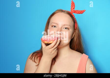 Surpoids jeune femme avec beignet sur fond de couleur. Concept de régime alimentaire Banque D'Images