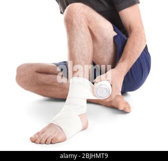 Jeune homme appliquant le bandage sur la jambe, sur fond blanc Banque D'Images