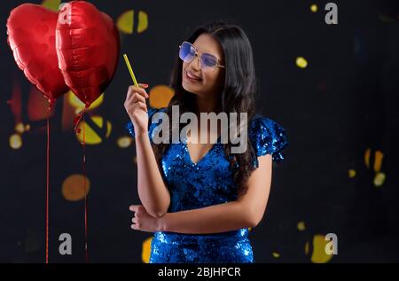 Jeune femme portant des lunettes de soleil colorées se tenant à côté de ballons en forme de coeur à une fête du nouvel an. Banque D'Images