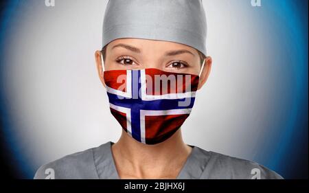 Norvège COVID-19 femme médecin portant un masque protecteur EPI avec drapeau norvégien pour la prévention du coronavirus. Portrait d'infirmière asiatique sur fond bleu confiant. Professionnel de la santé. Banque D'Images