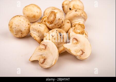 Moitiés de jeunes champignons coupés et de jeunes champignons dispersés sur un fond blanc. Gros plan Banque D'Images