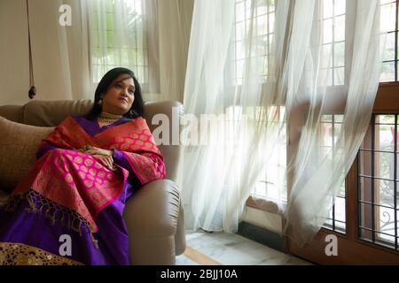 Une femme bien habillée assise confortablement sur un canapé à sa maison. Banque D'Images