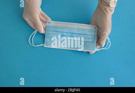 Mains dans des gants portant un masque médical sur le fond bleu Banque D'Images