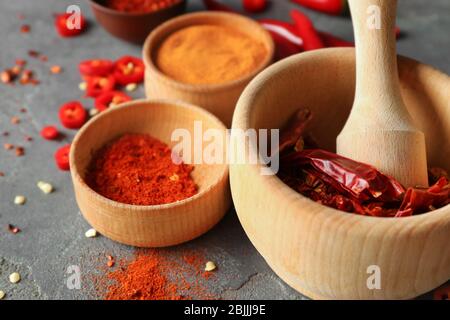 Poudre de piment rouge et poivrons secs dans du mortier de bois sur table grise Banque D'Images