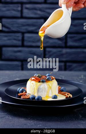 Un dessert de luxe cuit au four à fromage doux avec du pecan, des bleuets et du miel sur une plaque noire sur une table en béton devant une brique noire Banque D'Images